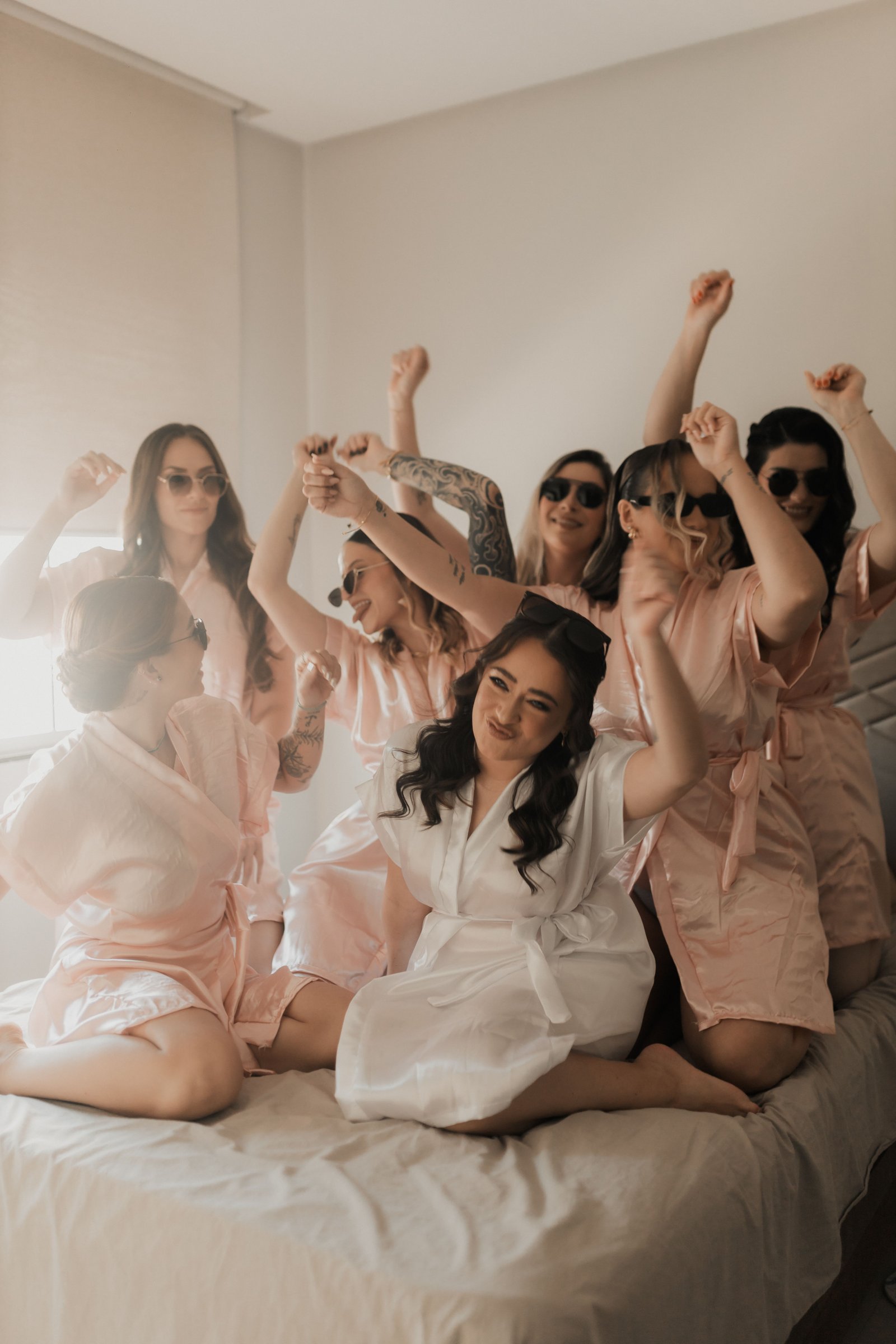 A joyful bridal party in robes celebrates during at home hair and makeup service before the wedding.