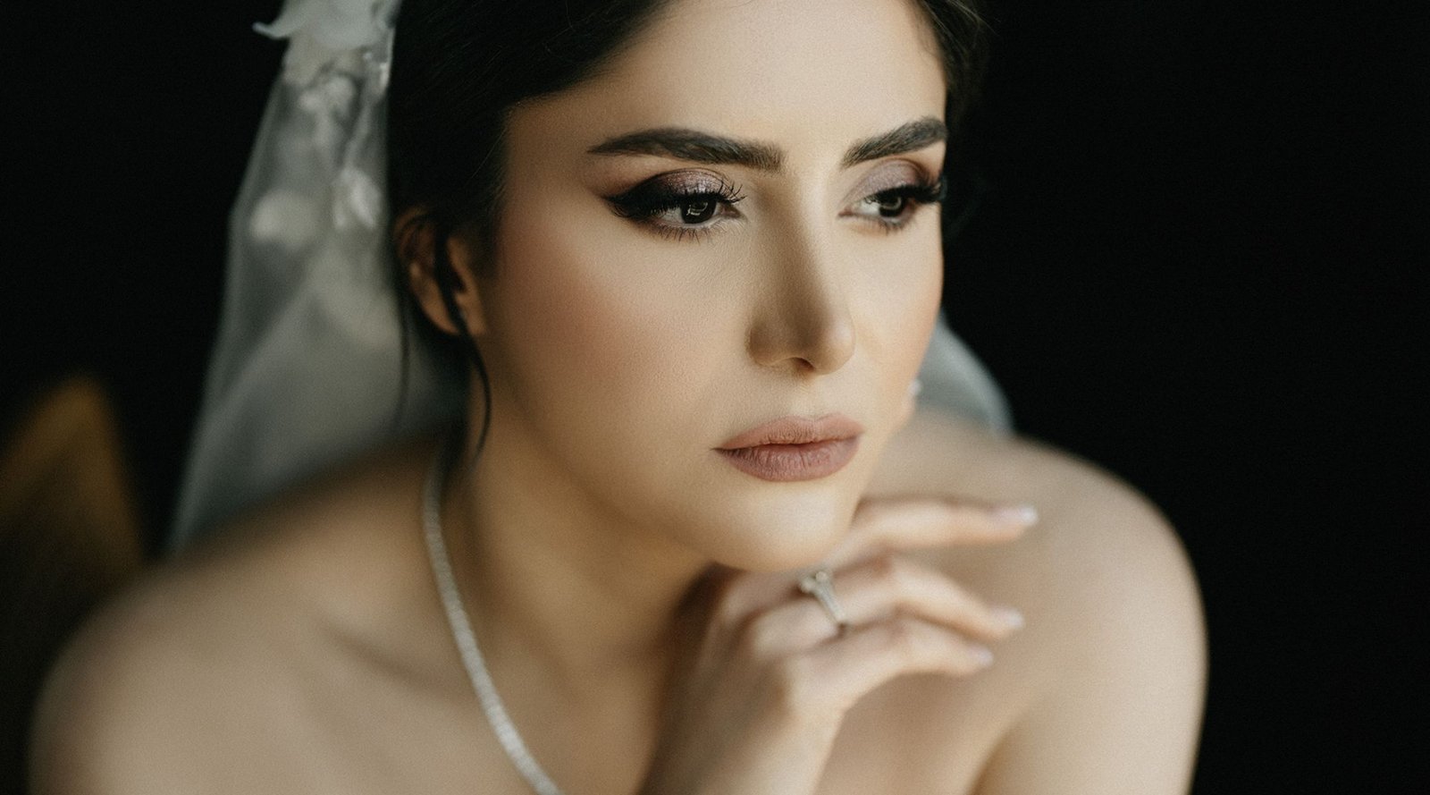 A close up portrait of a bride with soft bridal contouring makeup and a white veil.