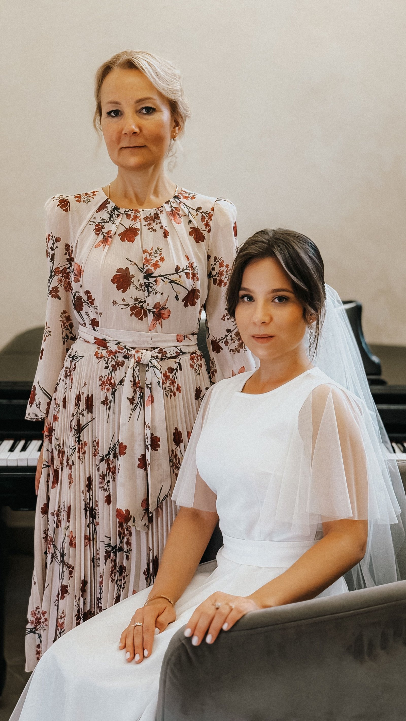 A mother of the bride wearing an elegant hairstyle and formal dress standing beside her daughter on the wedding day.