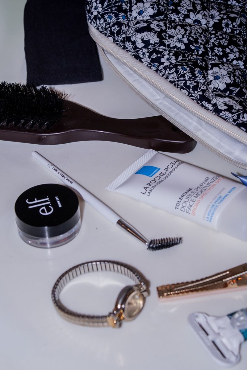 A flat lay of a small bridal cosmetics kit including a floral bag, brush, and travel size products.