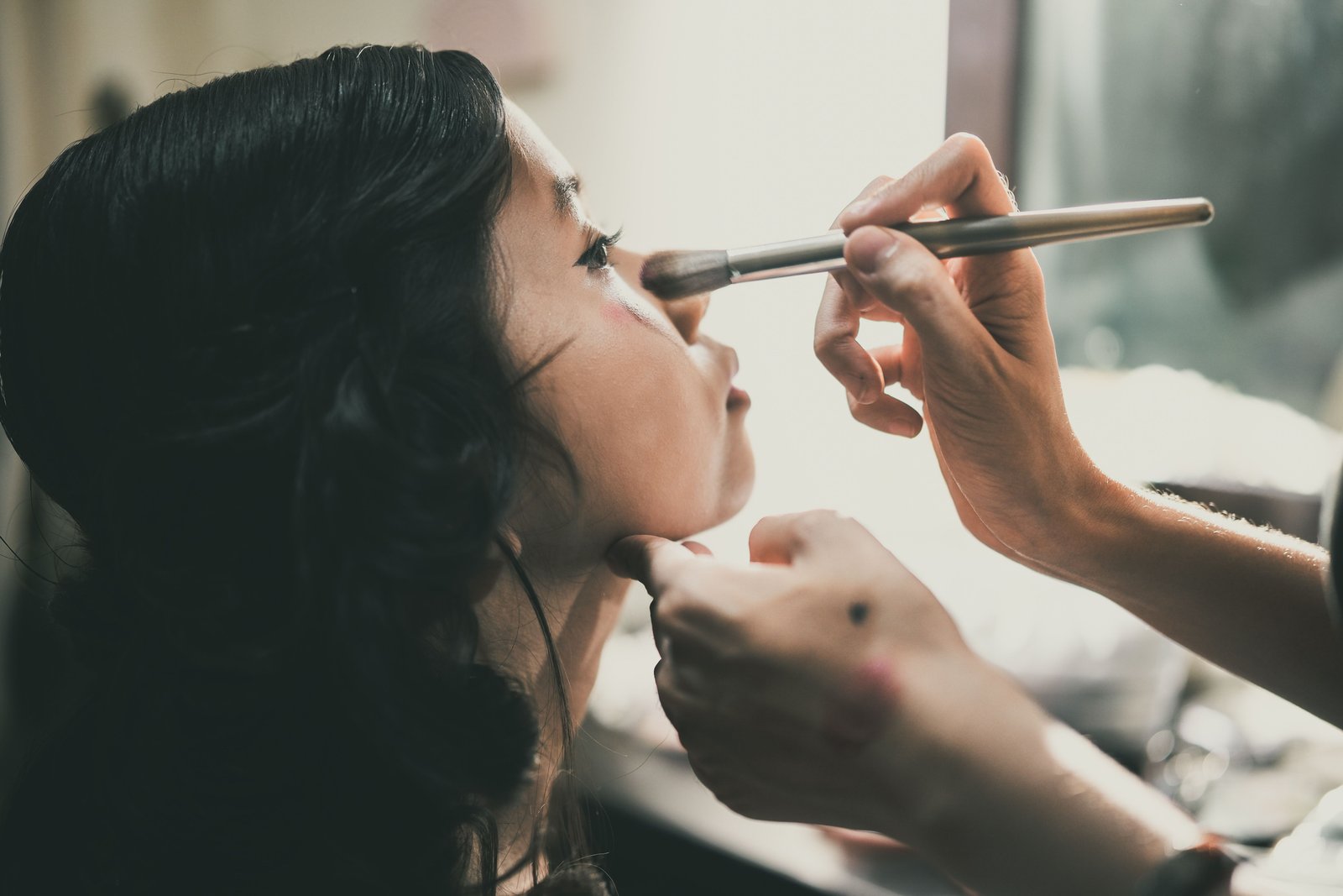 A professional makeup artist applying wedding makeup to a bride's face before her ceremony.