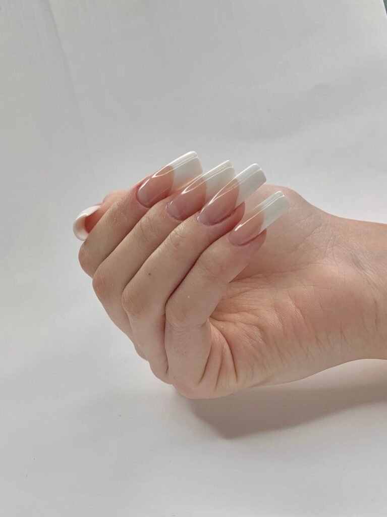 Hand with a fresh set of French tip press on nails, the kind attached with Kiss Pink Gel nail glue
