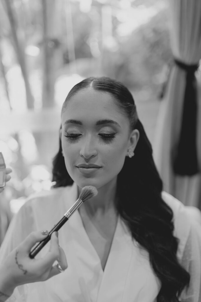 Makeup artist blending foundation makeup onto a bride's skin with a brush