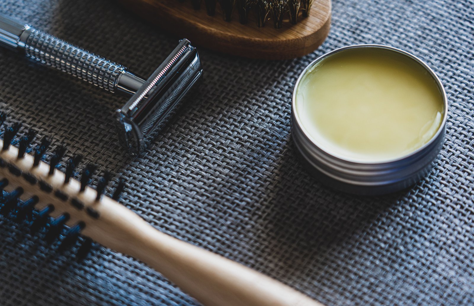 Flat lay of grooming tools including a razor, brush, and pomade tin