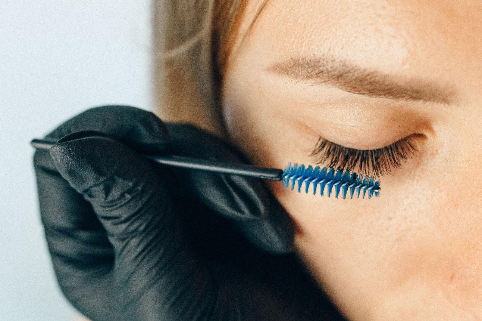 Lash technician using a fine applicator brush during a classic lash extension appointment