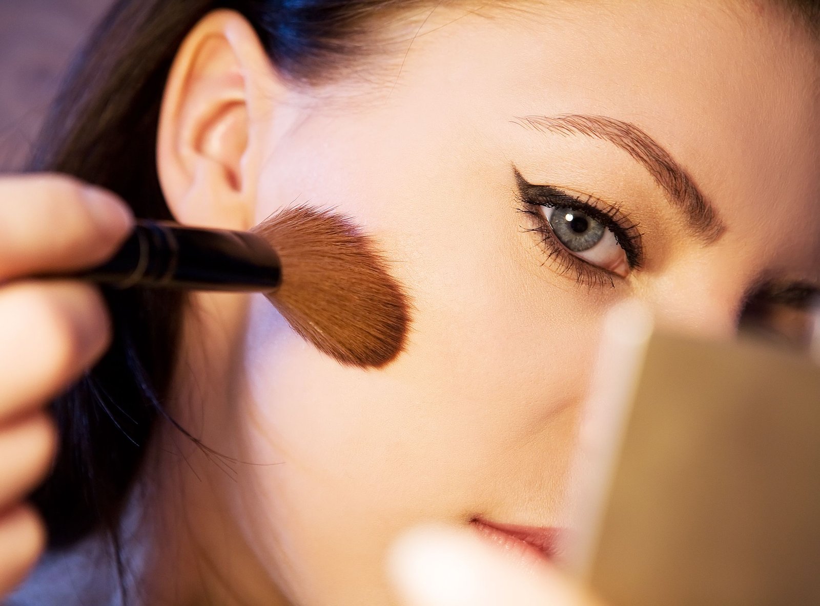 Close-up of blush being applied with a soft brush along the cheekbone