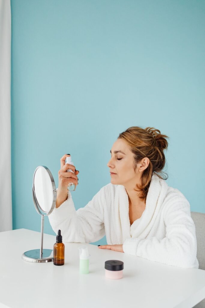 Woman lightly misting her face at a vanity with a setting spray that's good for her skin