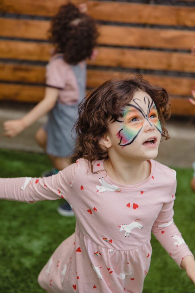Child with a butterfly face paint design playing at an outdoor celebration
