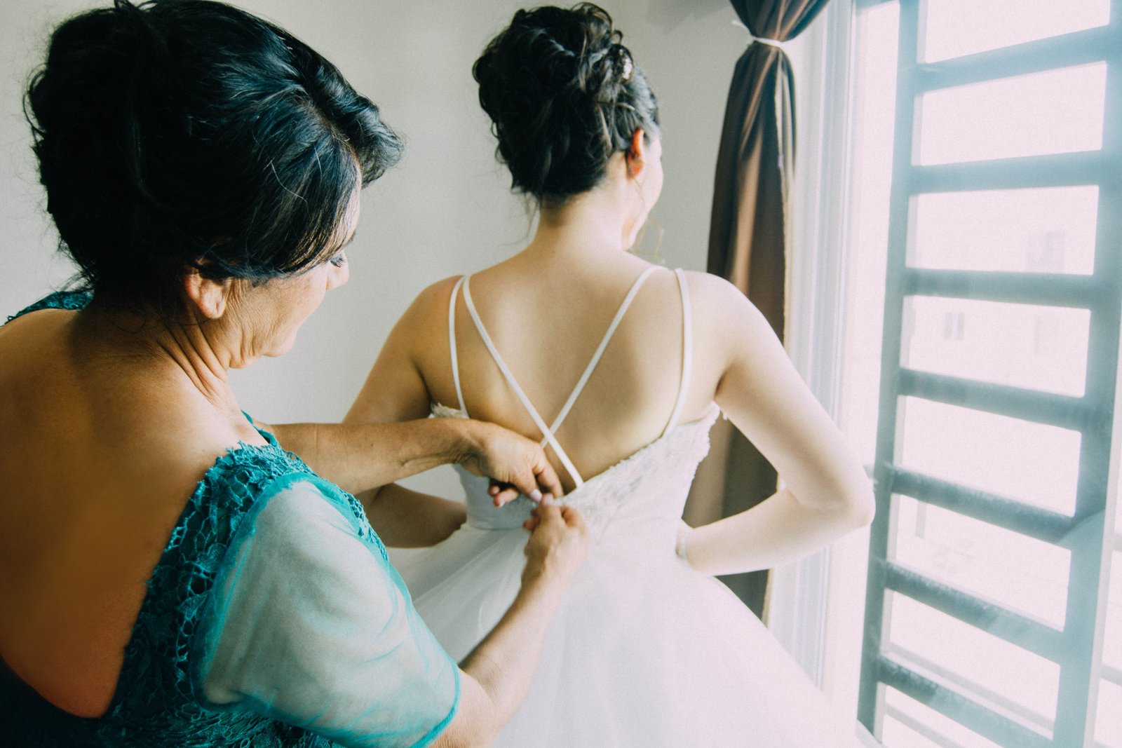Woman assisting a bride getting ready near a sunlit window